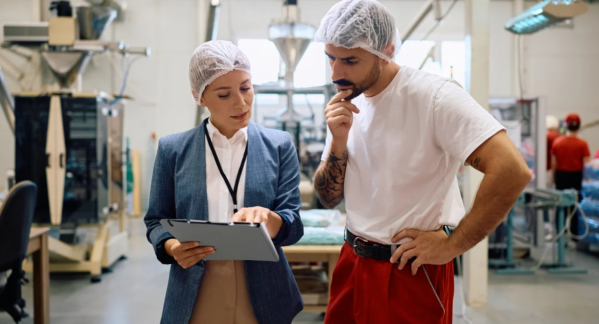 Quality control inspector and production line worker analyzing reports in a factory.