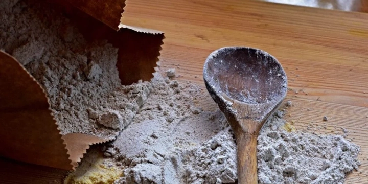 open bag of flour toppled over kitchen counter with wooden spoon in it