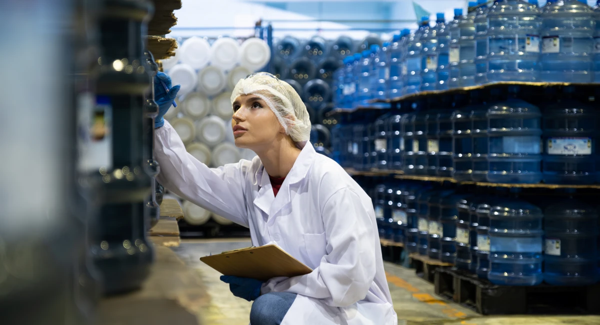  Caucasian women scientist with lab cote inspect quality of drinking water inside of the production line factory while using digital tablet to check cleanliness and standard, quality assurance