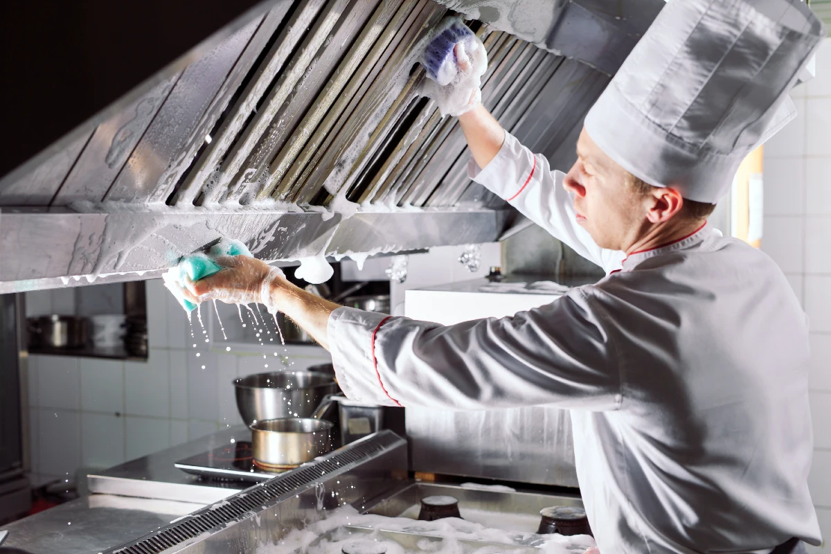 A chef cleaning the extractor in a restaurant kitchen