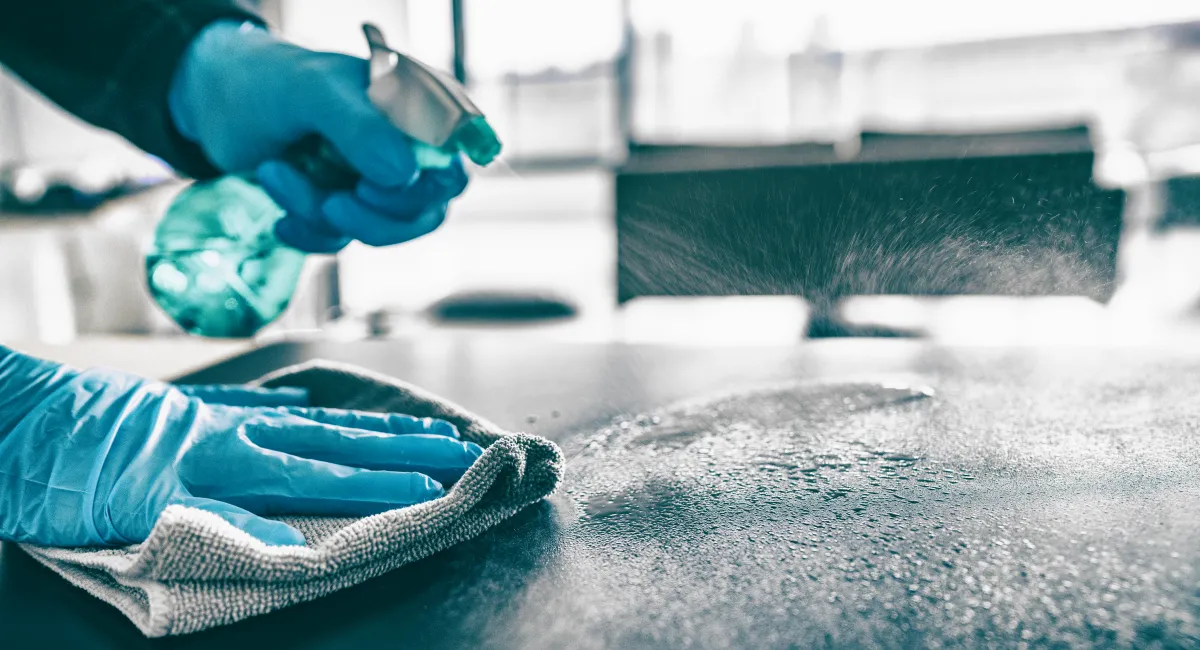 gloved hands spraying down and wiping table 