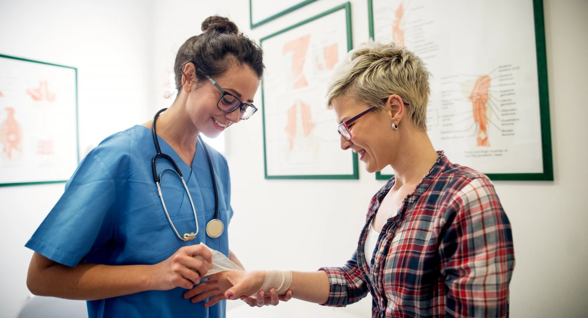 Female doctor bandaging up patient's hand in doctor office