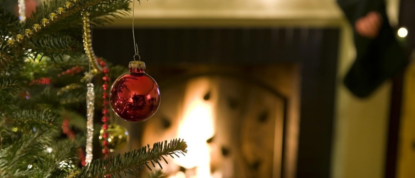 Close-up of a red ornament dangling on a Christmas tree in front of a fireplace