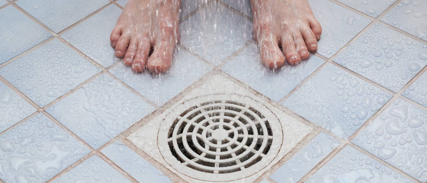Close-up of shower drain with someone standing beside it