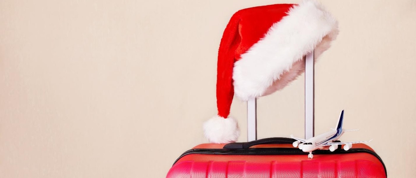 A Santa hat and miniature airplane resting on top of a red suitcase