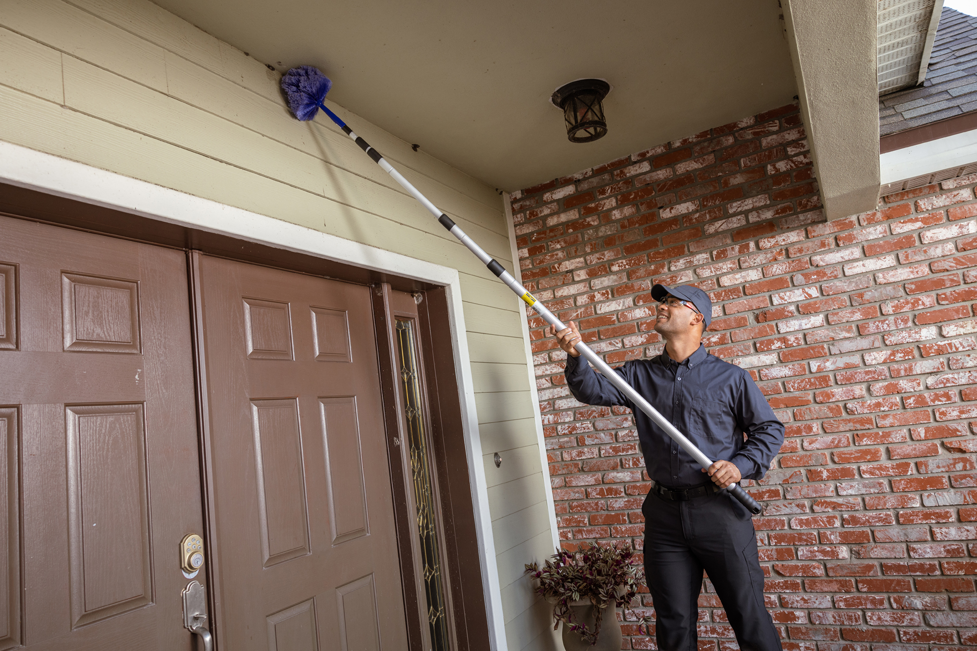 JP Pest Services technician removing cobwebs near the entry of an older multifamily building, addressing common pest access points around doors.