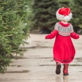 A small child dressed for the holidays runs through by a group of Christmas trees.