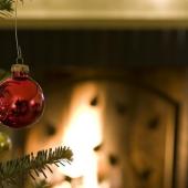 Close-up of a red ornament dangling on a Christmas tree in front of a fireplace
