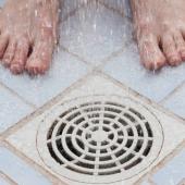 Close-up of shower drain with someone standing beside it