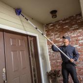  JP Pest Services technician removing cobwebs near the entry of an older multifamily building, addressing common pest access points around doors.