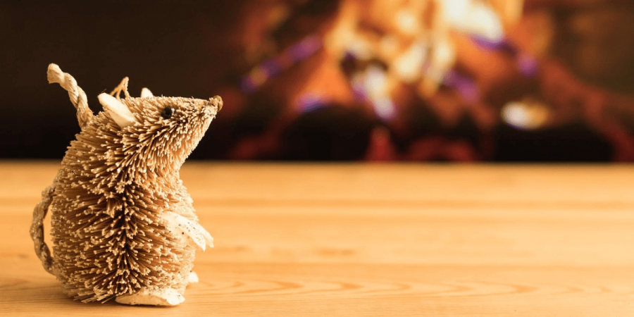 A small wicker mouse in front of a fireplace.