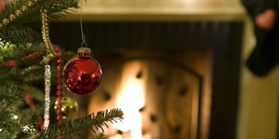 Close-up of a red ornament dangling on a Christmas tree in front of a fireplace