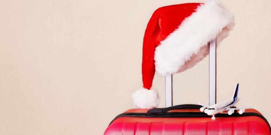 A Santa hat and miniature airplane resting on top of a red suitcase