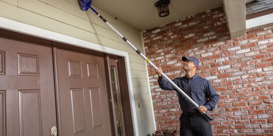  JP Pest Services technician removing cobwebs near the entry of an older multifamily building, addressing common pest access points around doors.