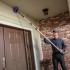  JP Pest Services technician removing cobwebs near the entry of an older multifamily building, addressing common pest access points around doors.